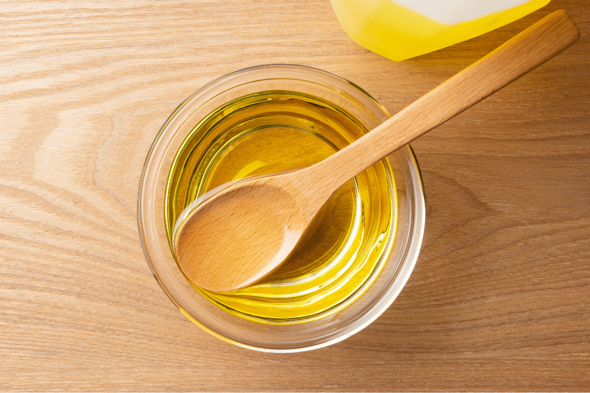Vegetable oil in a glass bowl with a wooden spoon in it.