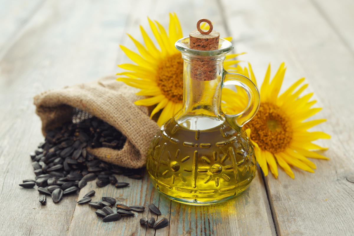A glass jar of sunflower oil with a small sack full of sunflower seeds and sunflowers on the side.