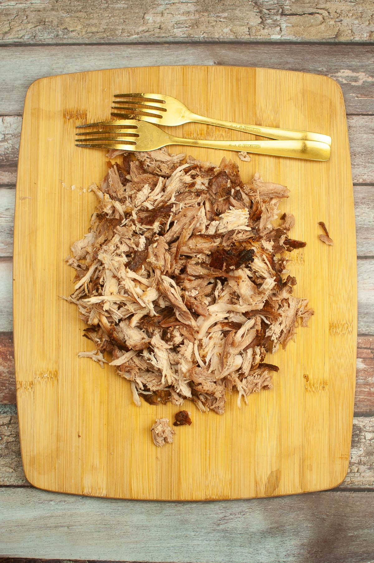 Shredded pork on a wooden board with two forks on the side.