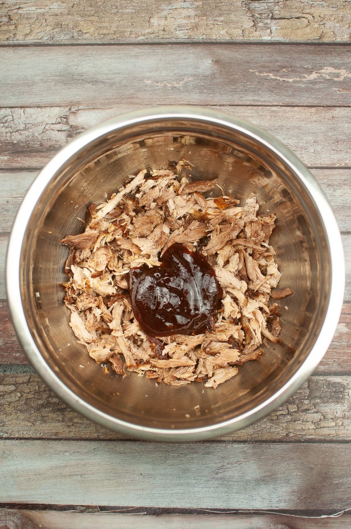 Shredded pork in a mixing bowl with BBQ sauce.