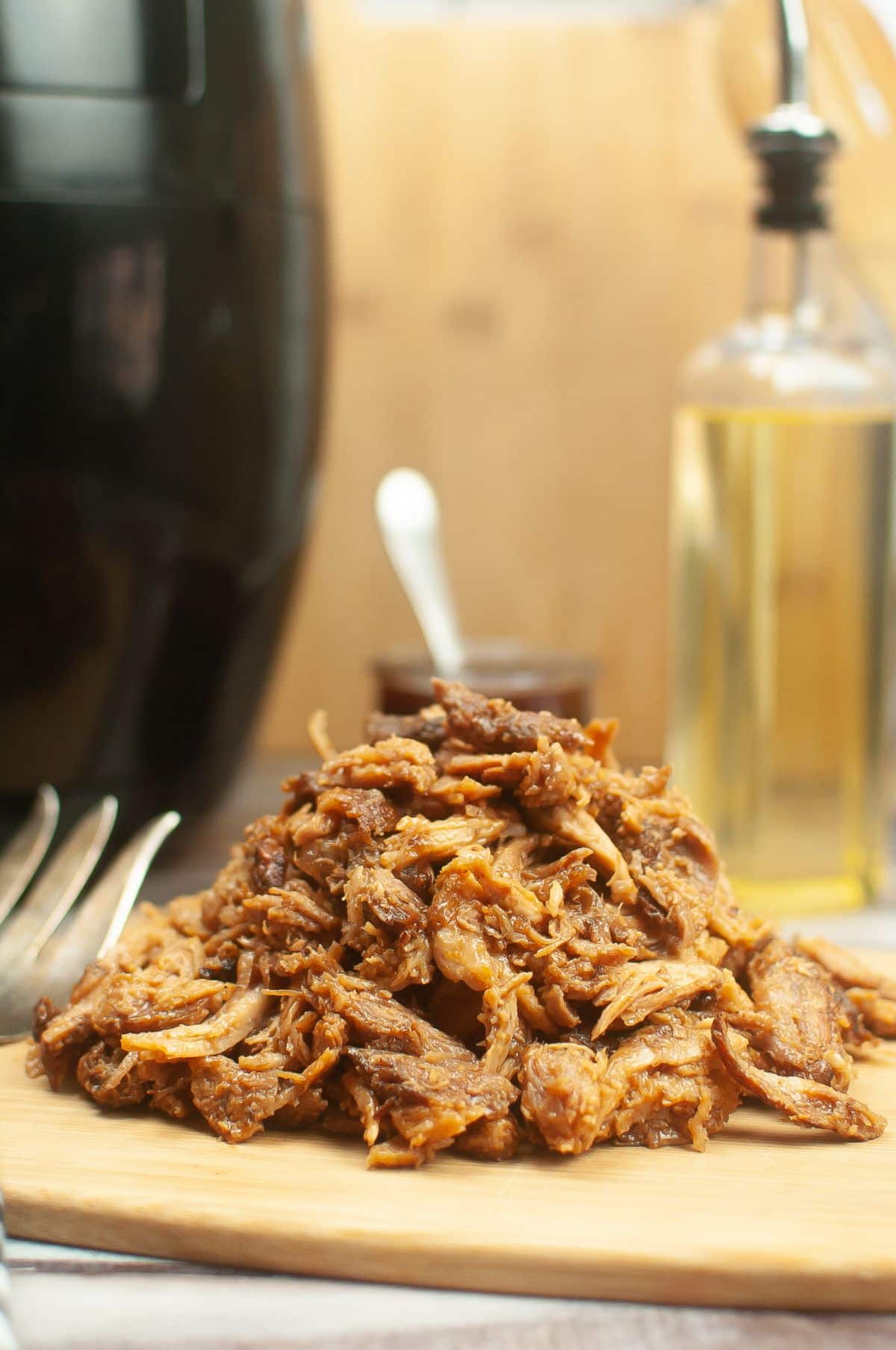 Air Fryer Pulled Pork on a wooden board, Air Fryer, BBQ sauce, olive oil, fork on the side.