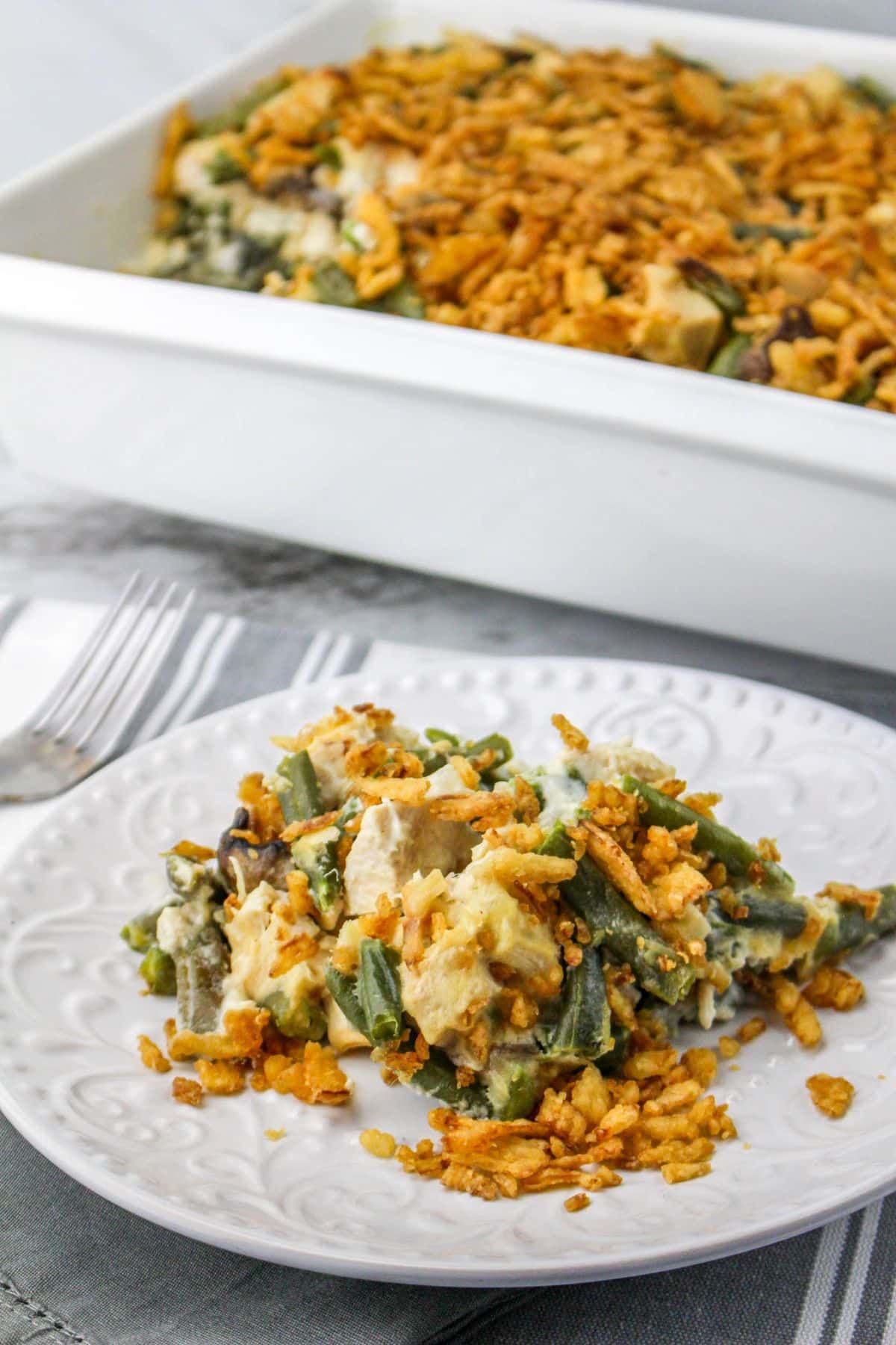 Green Bean Chicken Casserole on a serving plate with fork and casserole dish on the side.