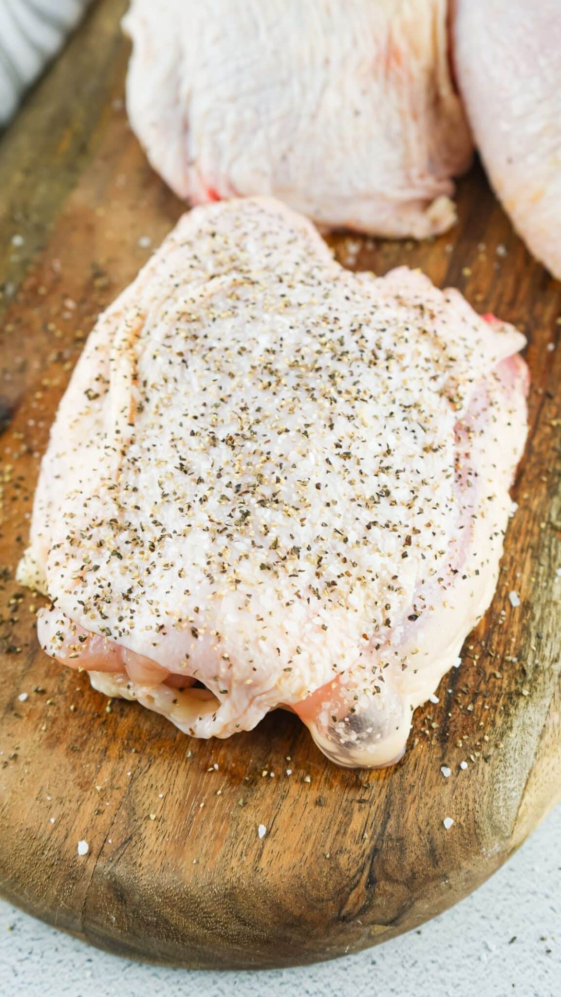 Chicken thighs are being seasoned with salt and black pepper.