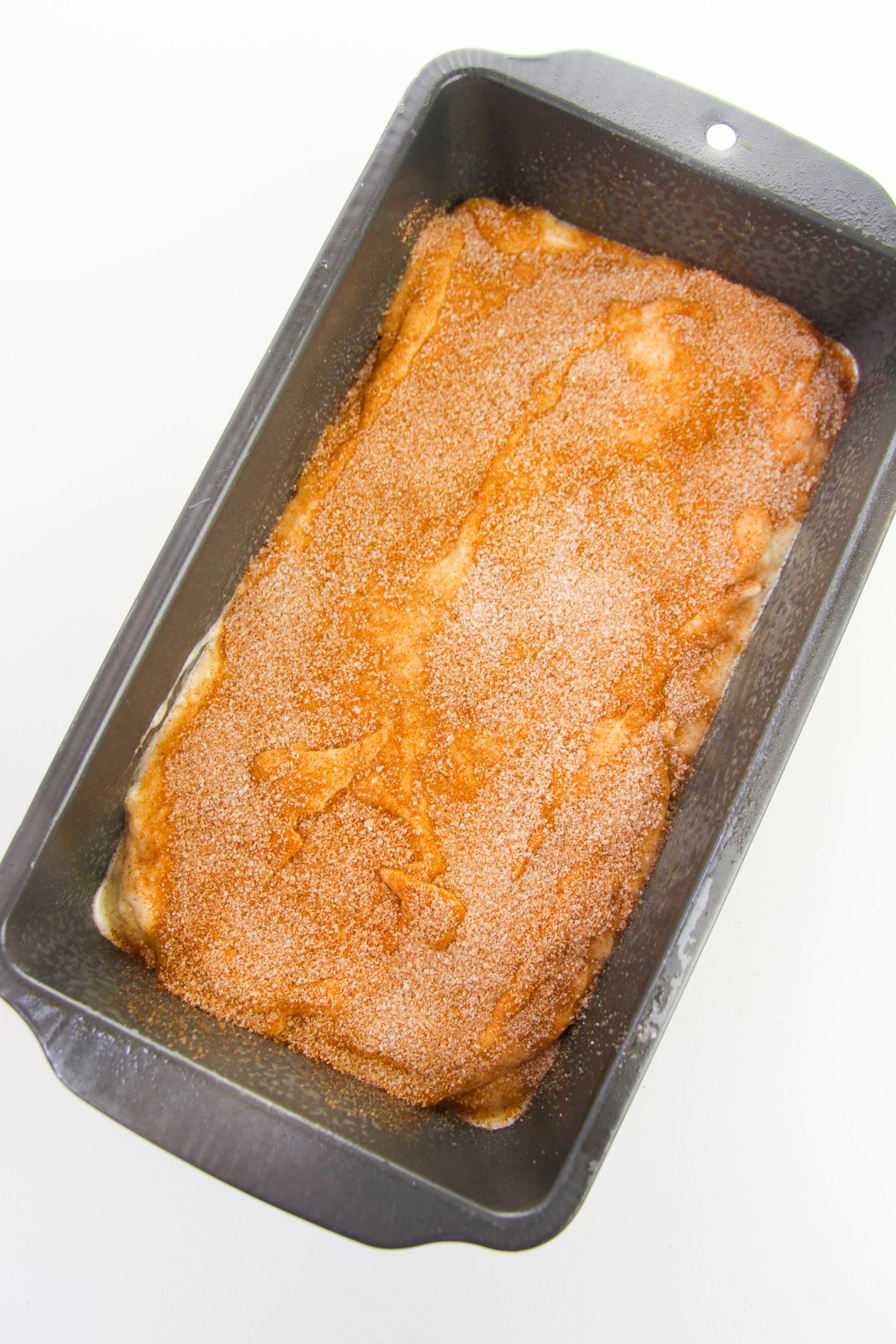 Loaf pan filled with banana batter and sprinkled with cinnamon and sugar.
