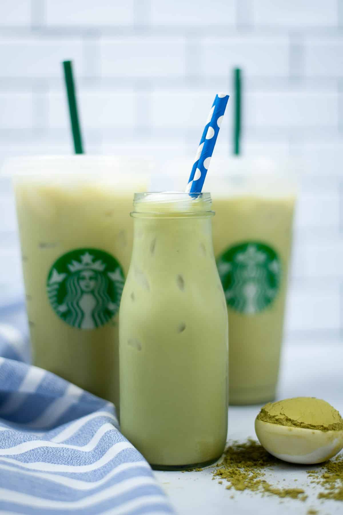 Copycat Starbucks Matcha Green Tea Latte in a bottle with straw, more latte cups in background.