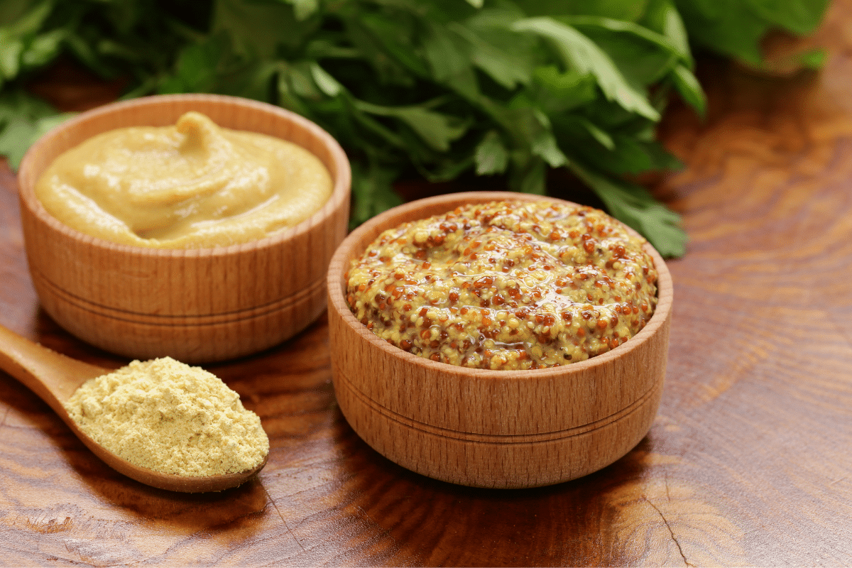 Ground and sauce mustard in a wooden bowl with mustard powder on a wooden spoon on the side.
