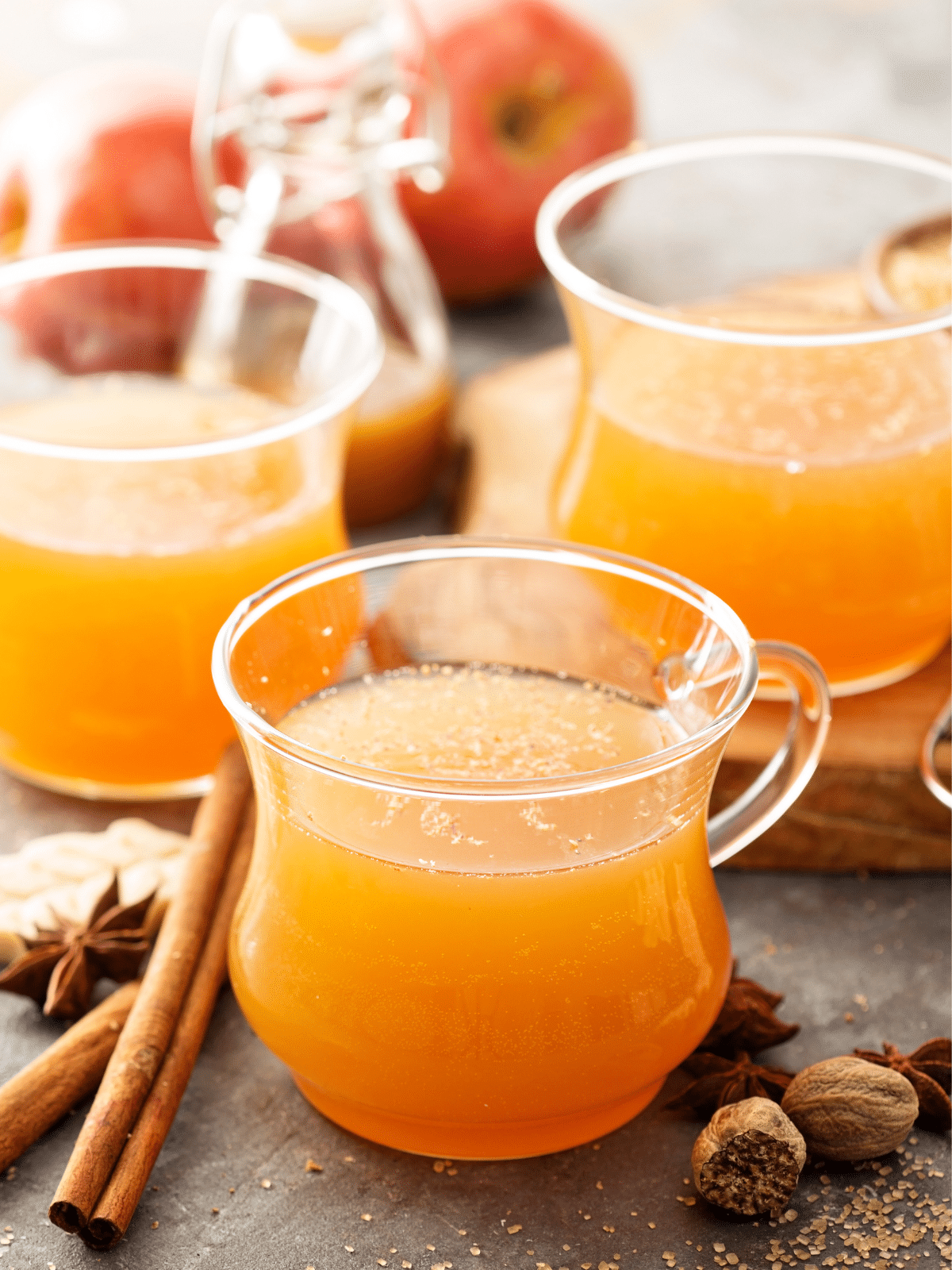 Three cups of apple cider, cinnamon, star anise and apples on the side.