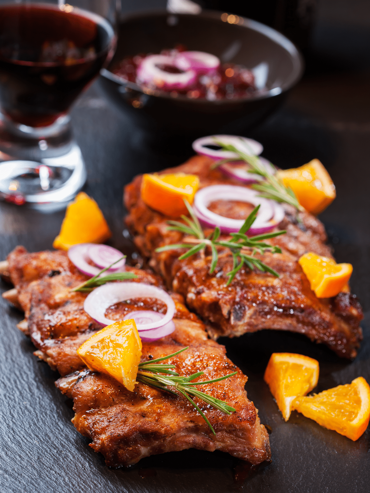 BBQ spare ribs marinated with orange juice, garnished with onions, rosemary, and sliced orange.