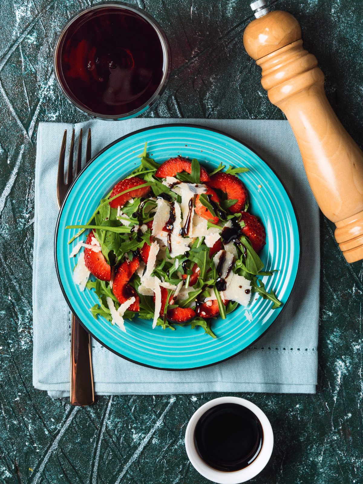 Strawberry salad drizzled with balsamic vinegar, with fork, pepper, and a bowl of balsamic vinegar on the side.