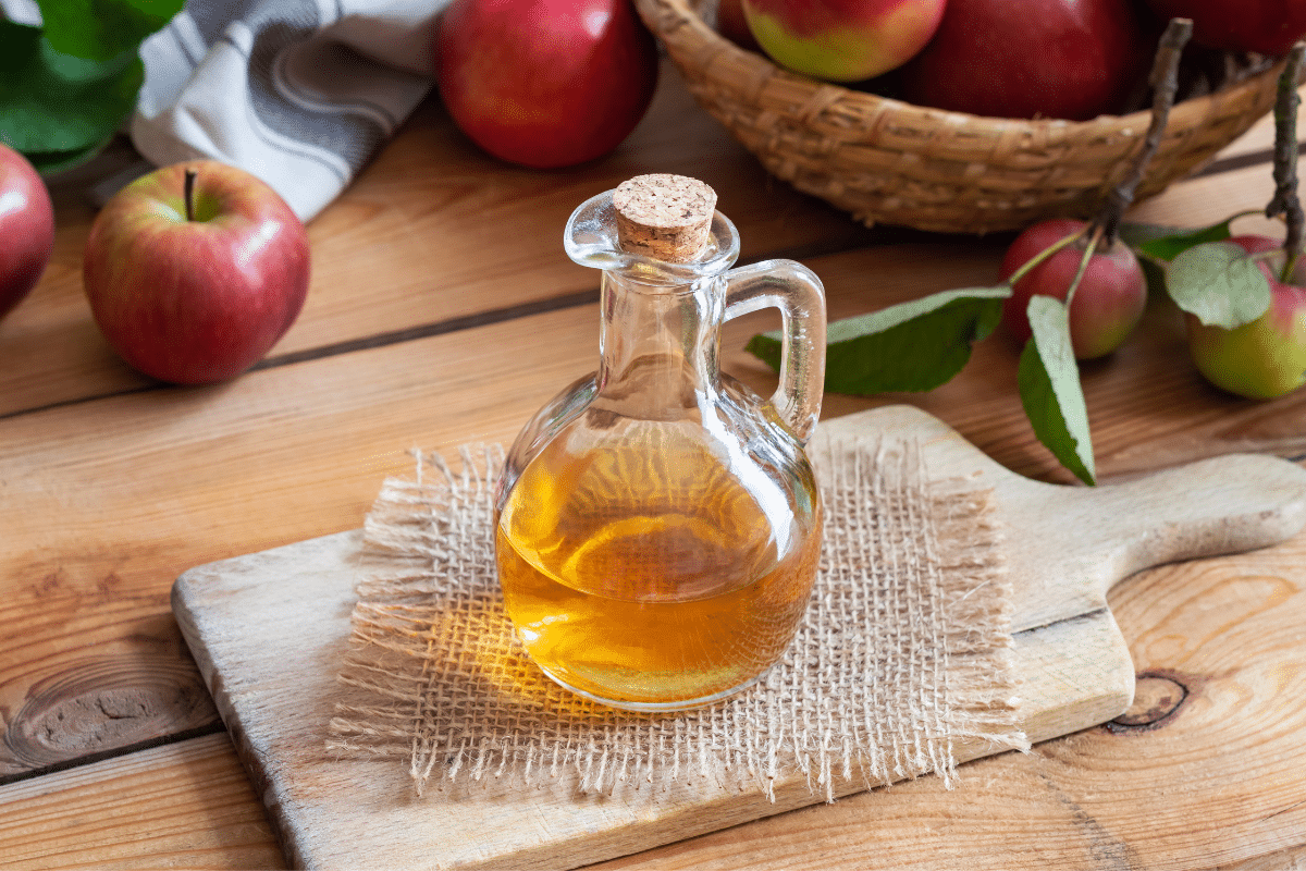 Apple cider vinegar in a bottle on a wooden board with a basket of apples on the side.