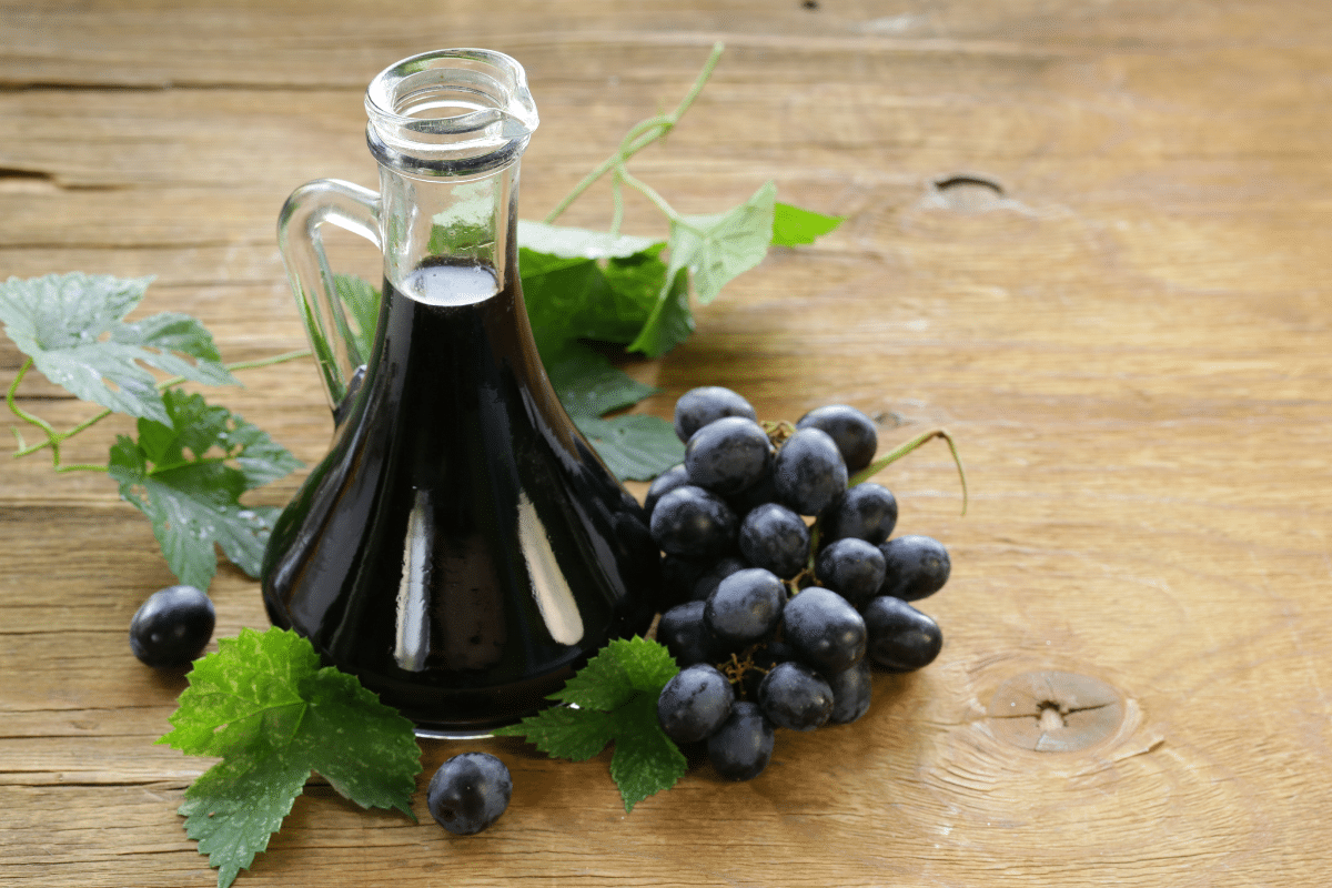 A bottle of balsamic vinegar on a wooden table with grapes on the side.
