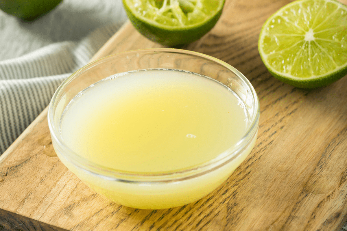 Bowl full of freshly squeezed lime juice on a wooden board.