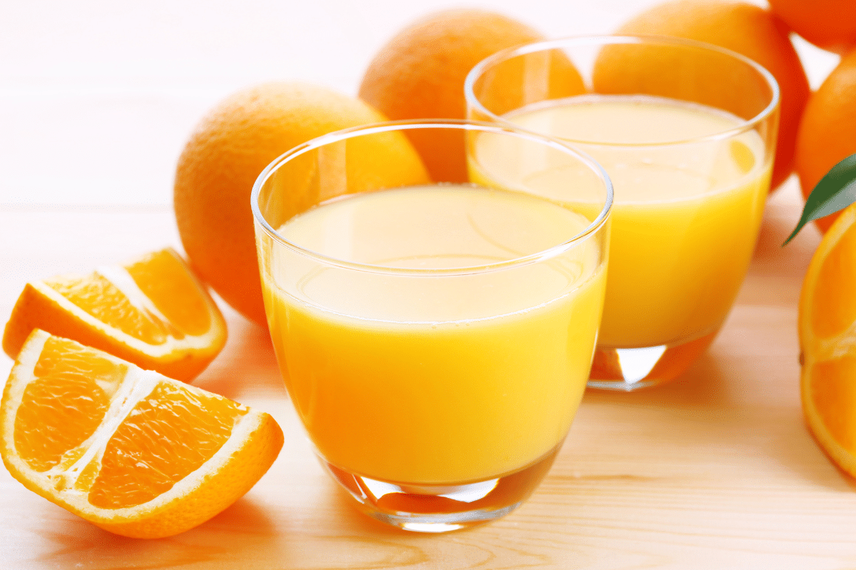 Two cups of orange juice, with fresh oranges on the side.
