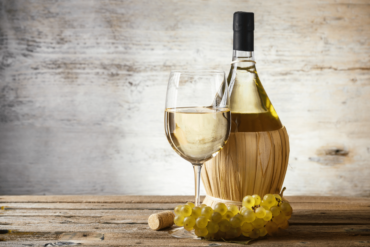 Bottle and glass of white wine with white grapes on the side.