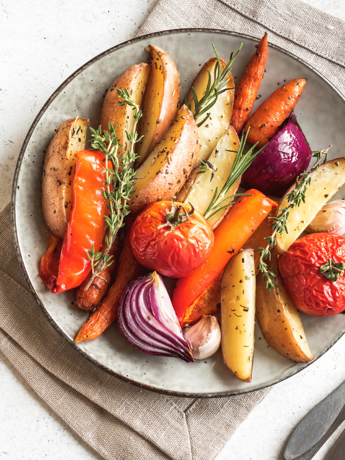 Roasted seasonal vegetables on a serving plate with fresh thyme and rosemary.