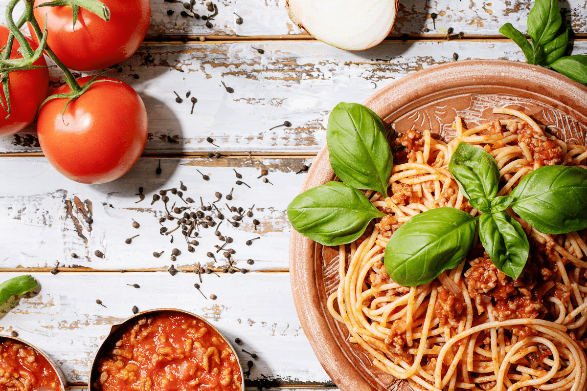 Spaghetti Bolognese in ceramic plate with fresh basil on top, tomatoes and sauce on the side.