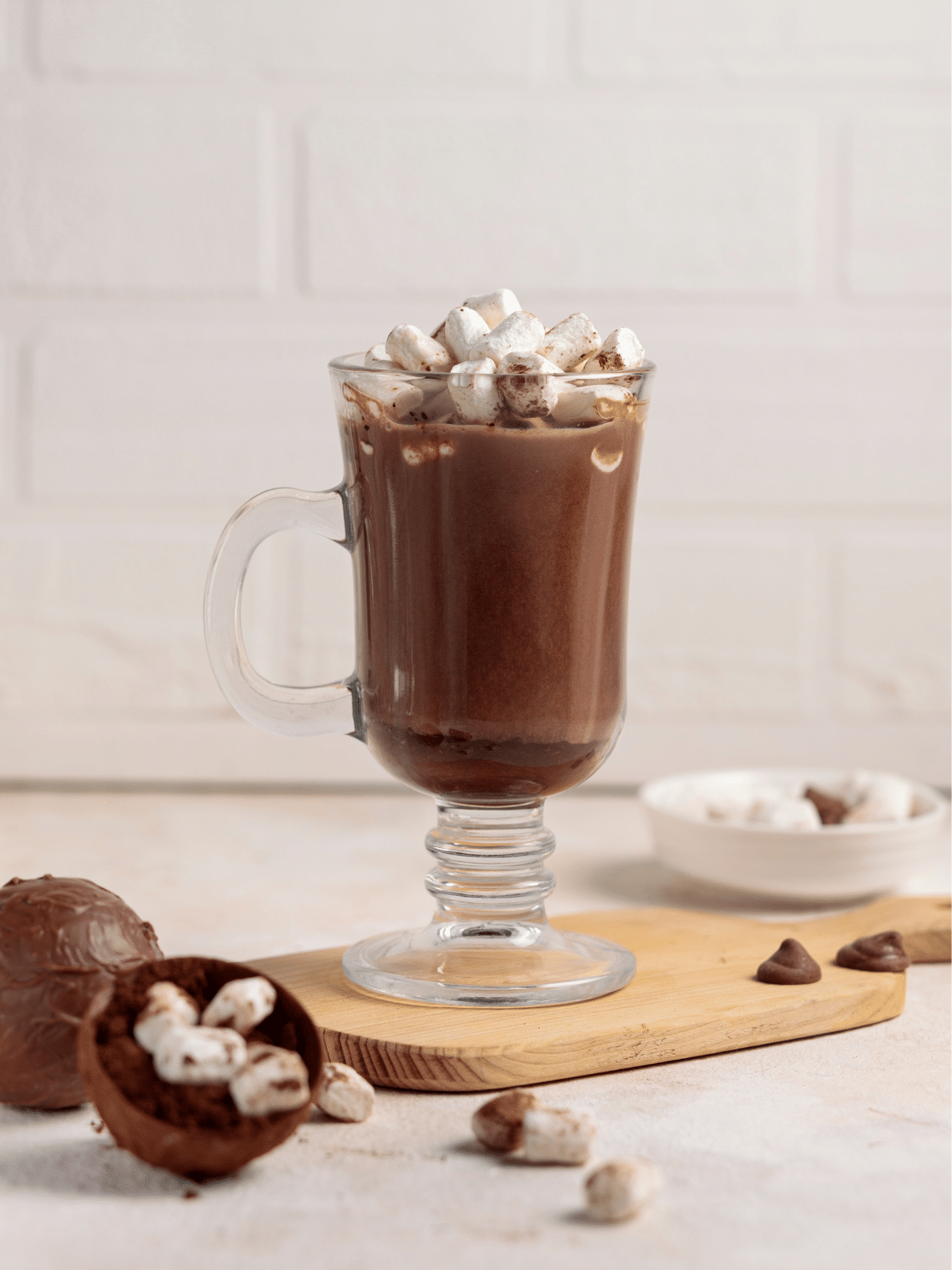 Hot cocoa bomb in a serving glass topped with marshmallows on a wooden board.