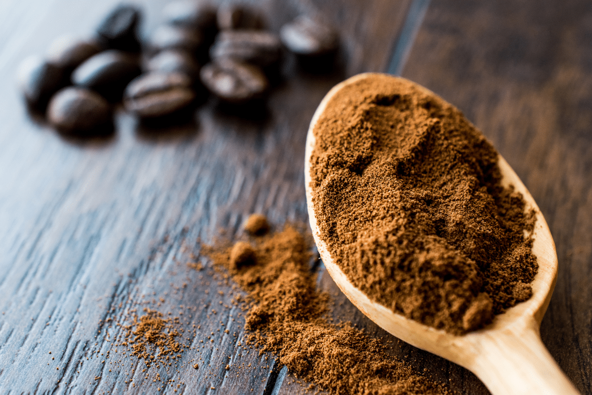 Espresso Powder on a wooden spoon, with coffee beans on the side.