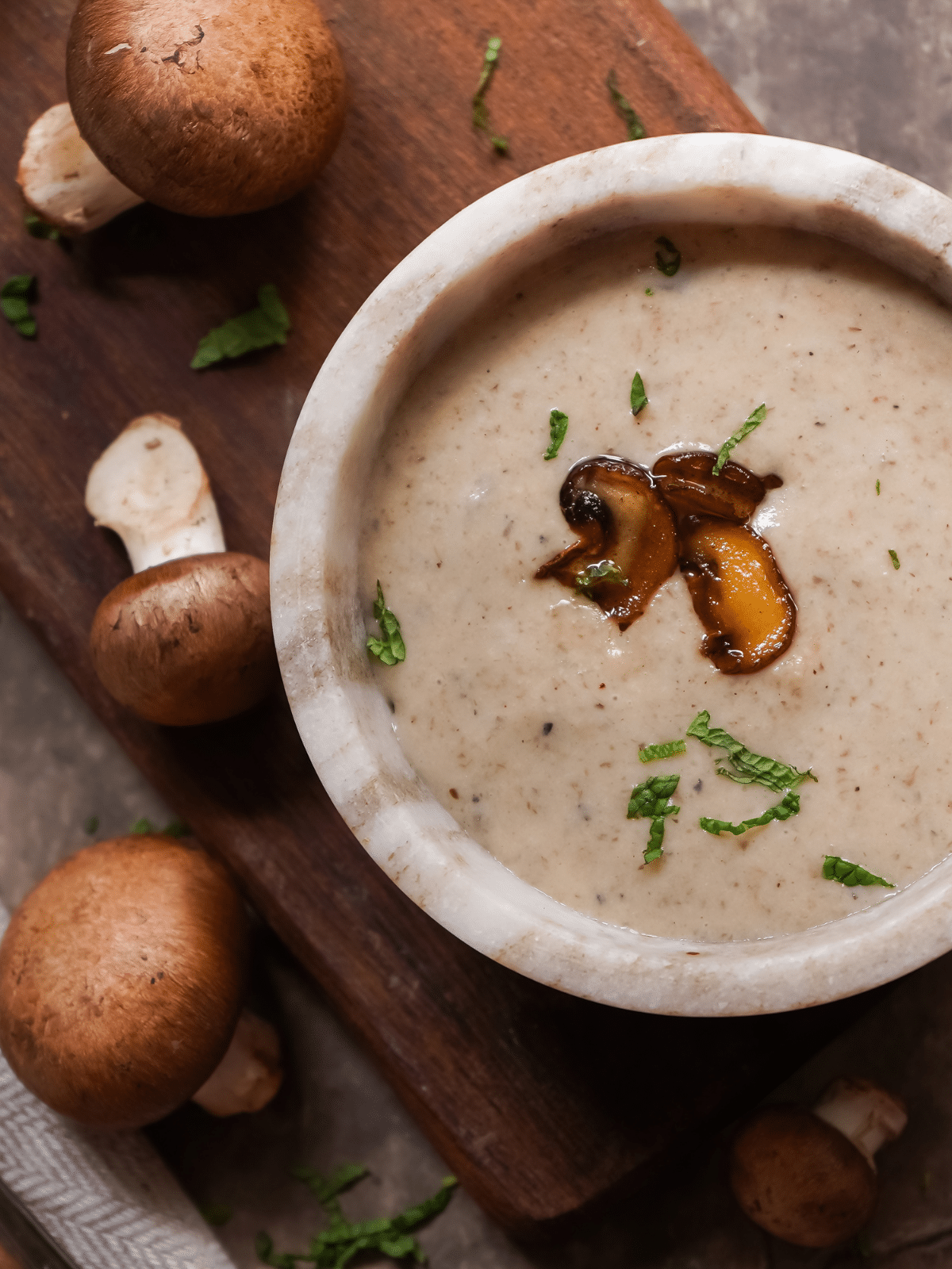 A bowl of cream of mushroom soup on a wooden board with mushrooms on the side.