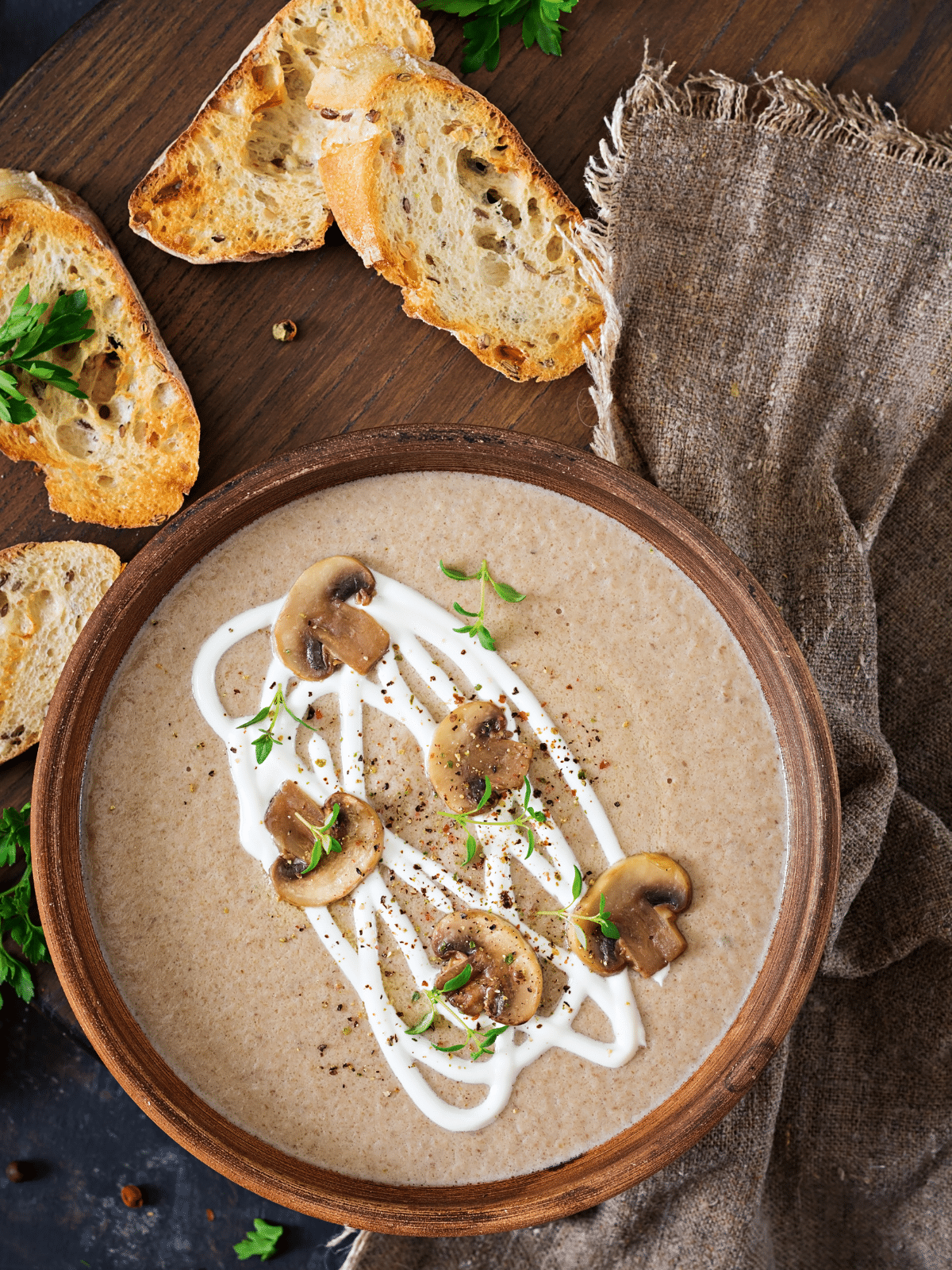 A bowl of cream of mushroom soup on a wooden table, Toasted sliced bread on the side.