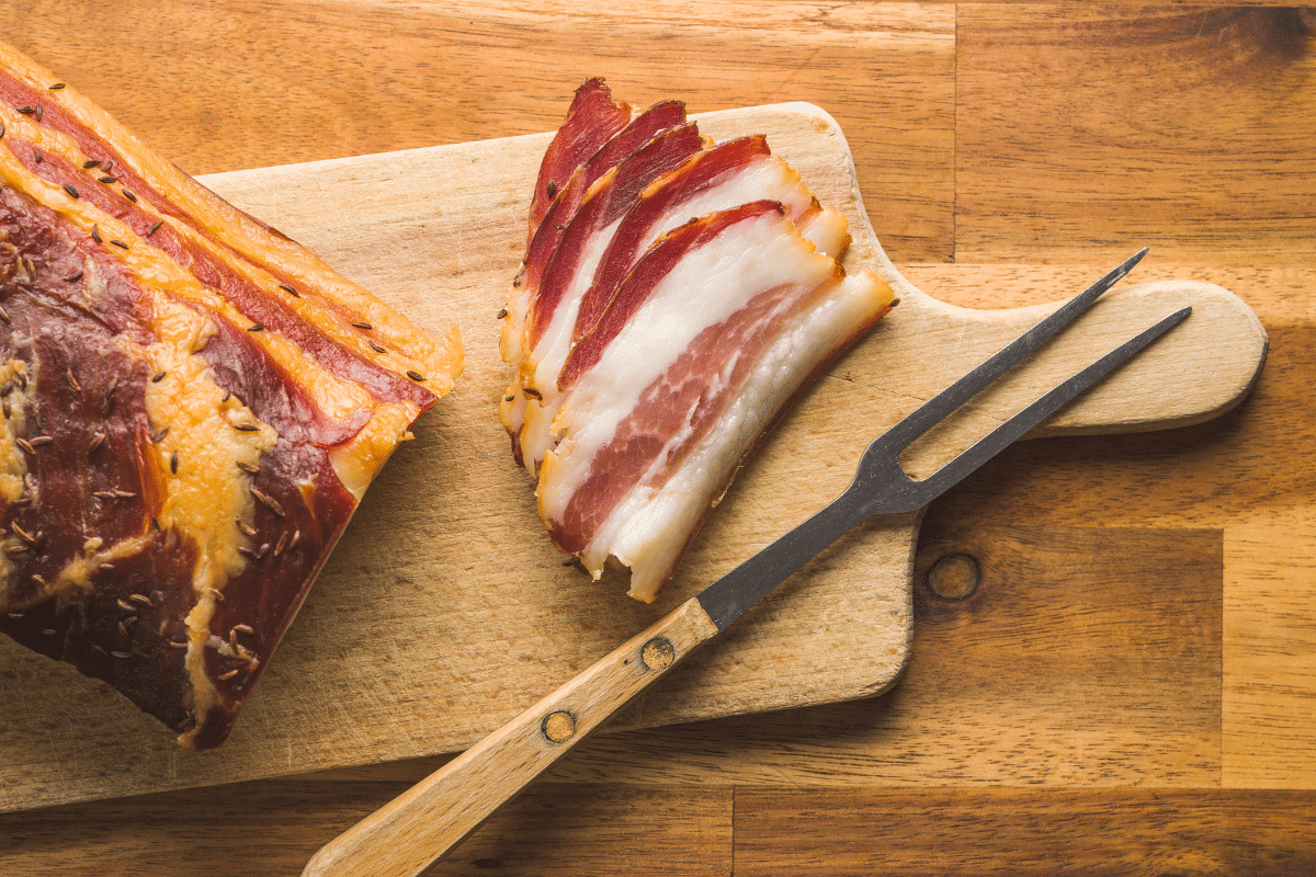 Smoked bacon on a wooden board with skewer fork on the side.