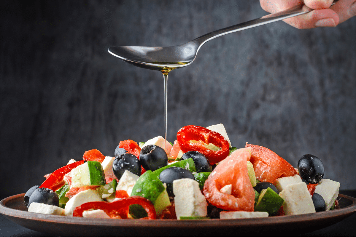 Greek salad with oil pouring from spoon above it.