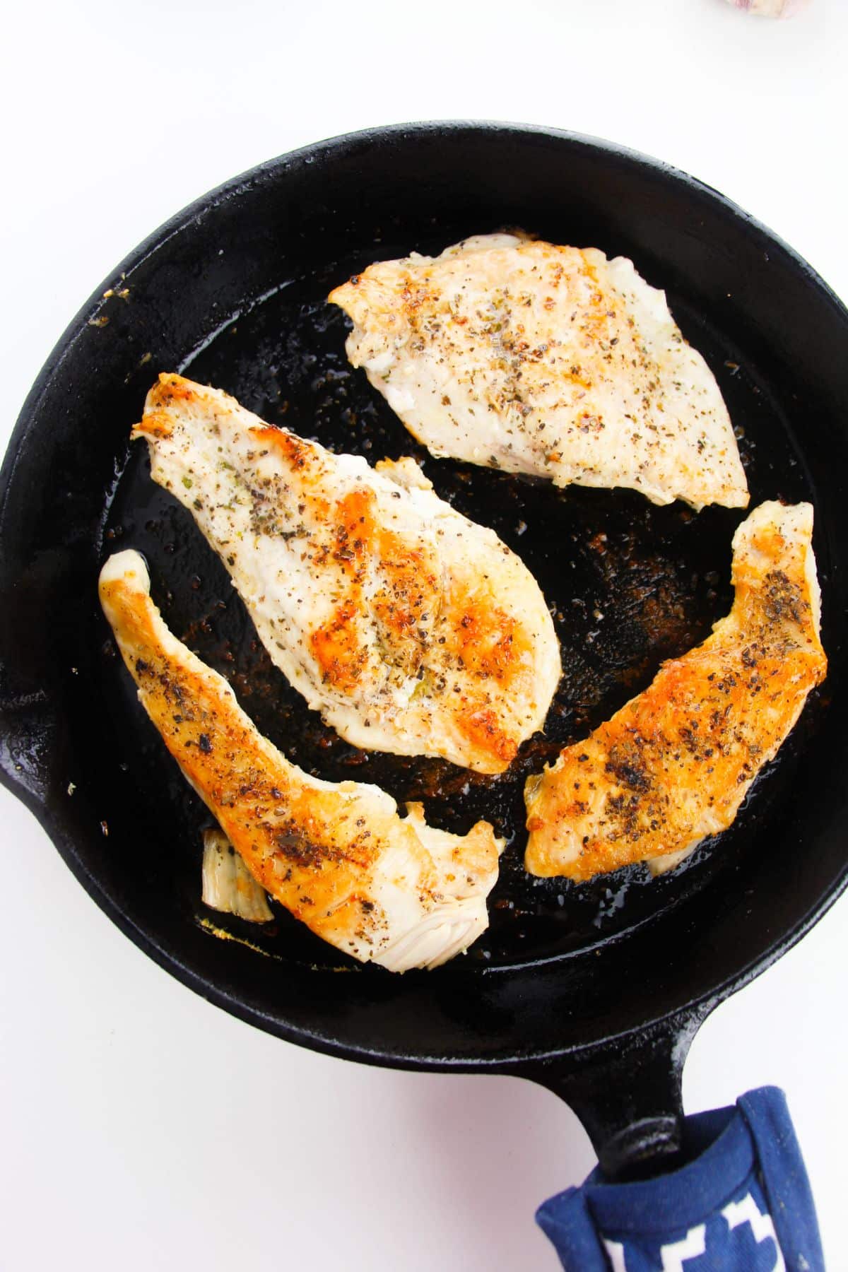 The chicken breasts are being seared in a skillet.