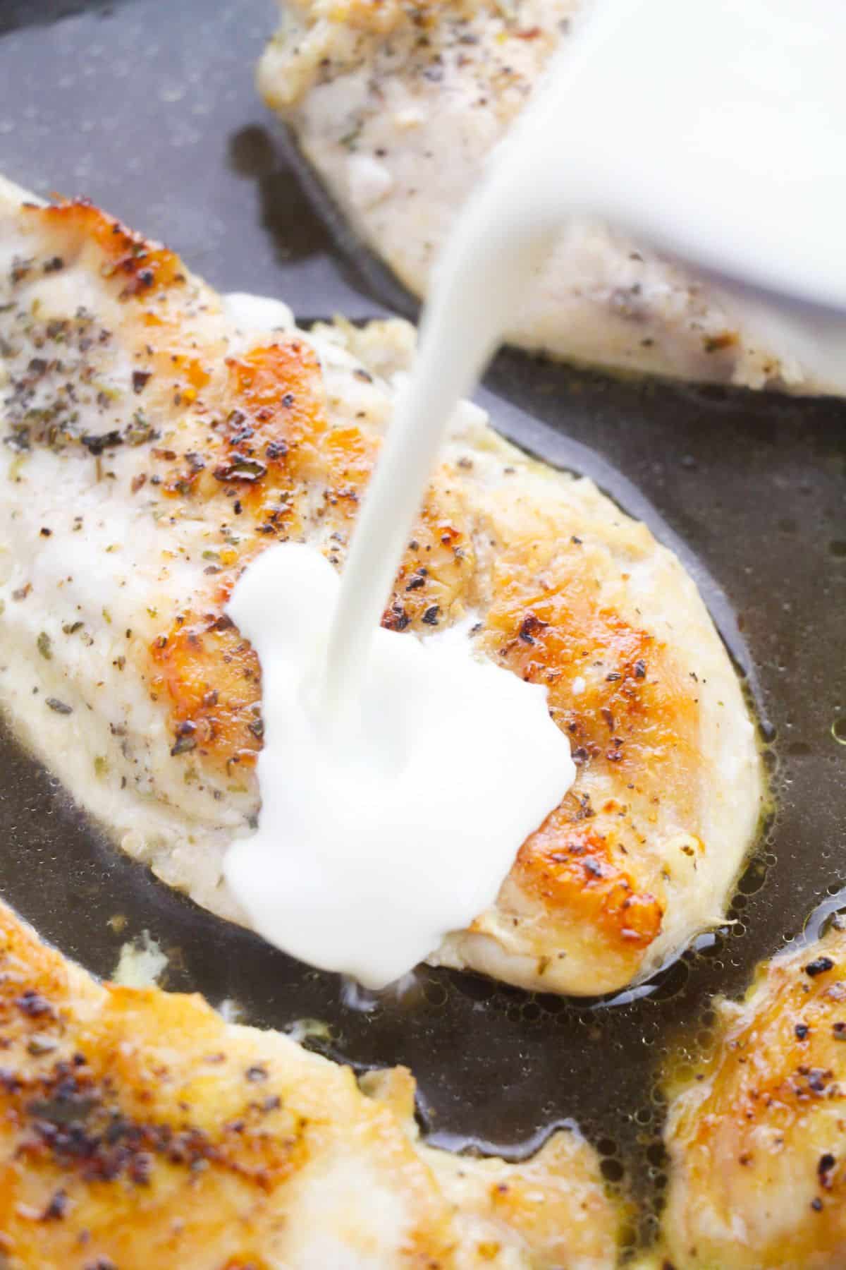 Heavy whipping cream is added to the chicken breasts cooking in a skillet.