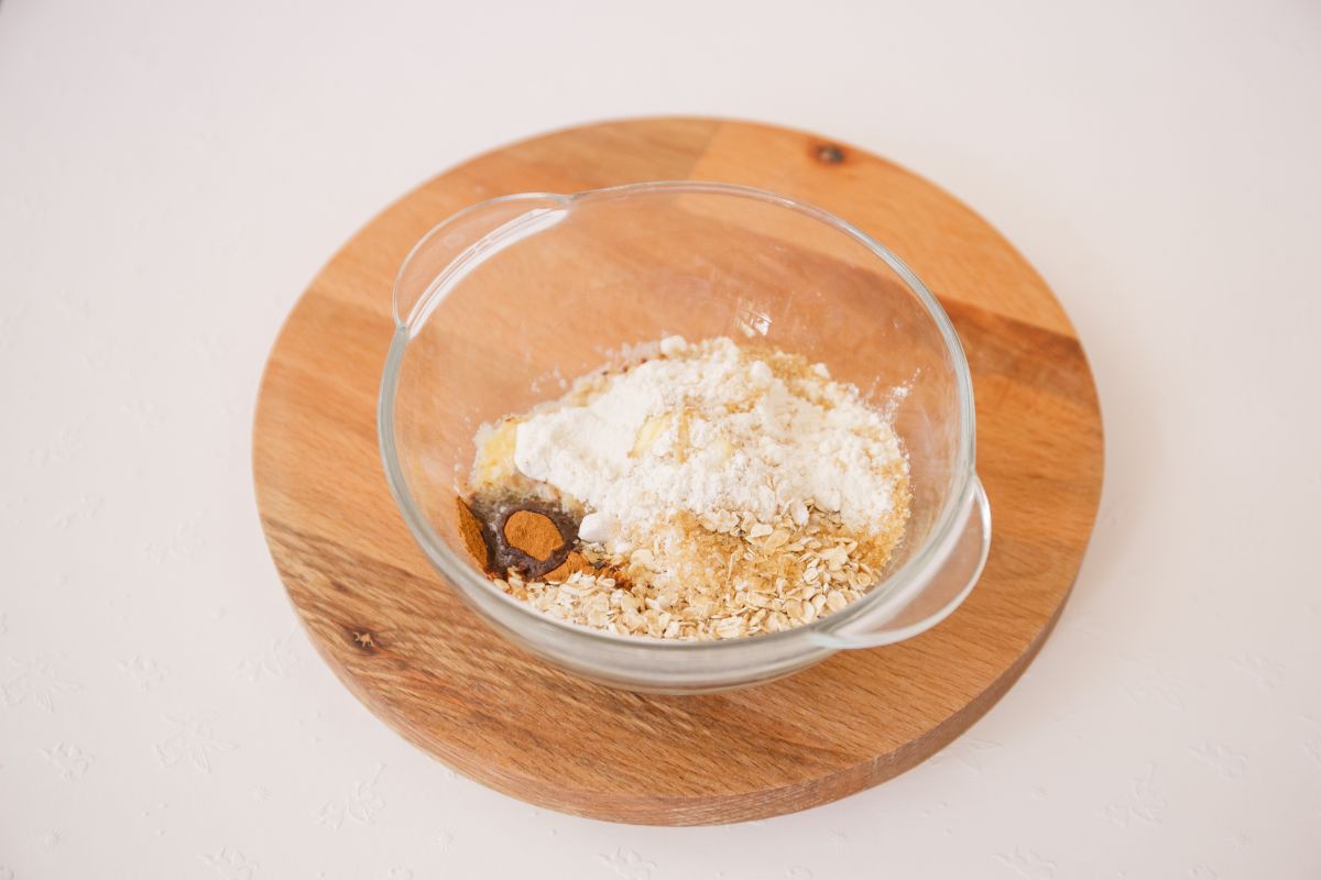 Oatmeal, flour, brown sugar, cinnamon, and melted butter in a glass mixing bowl on a wooden board.