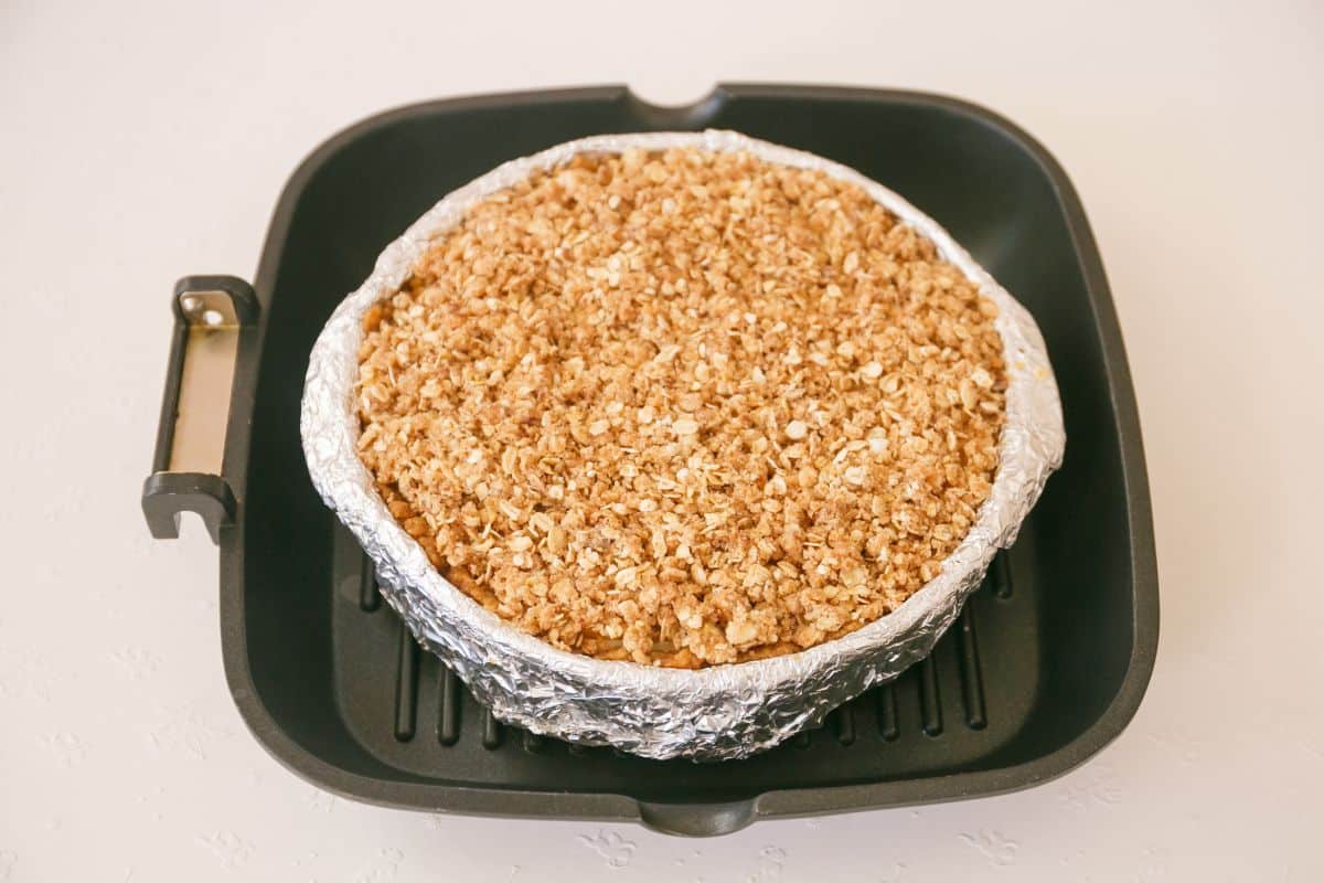 Apple crumble cheesecake topped with crumbs in a large frying pan.