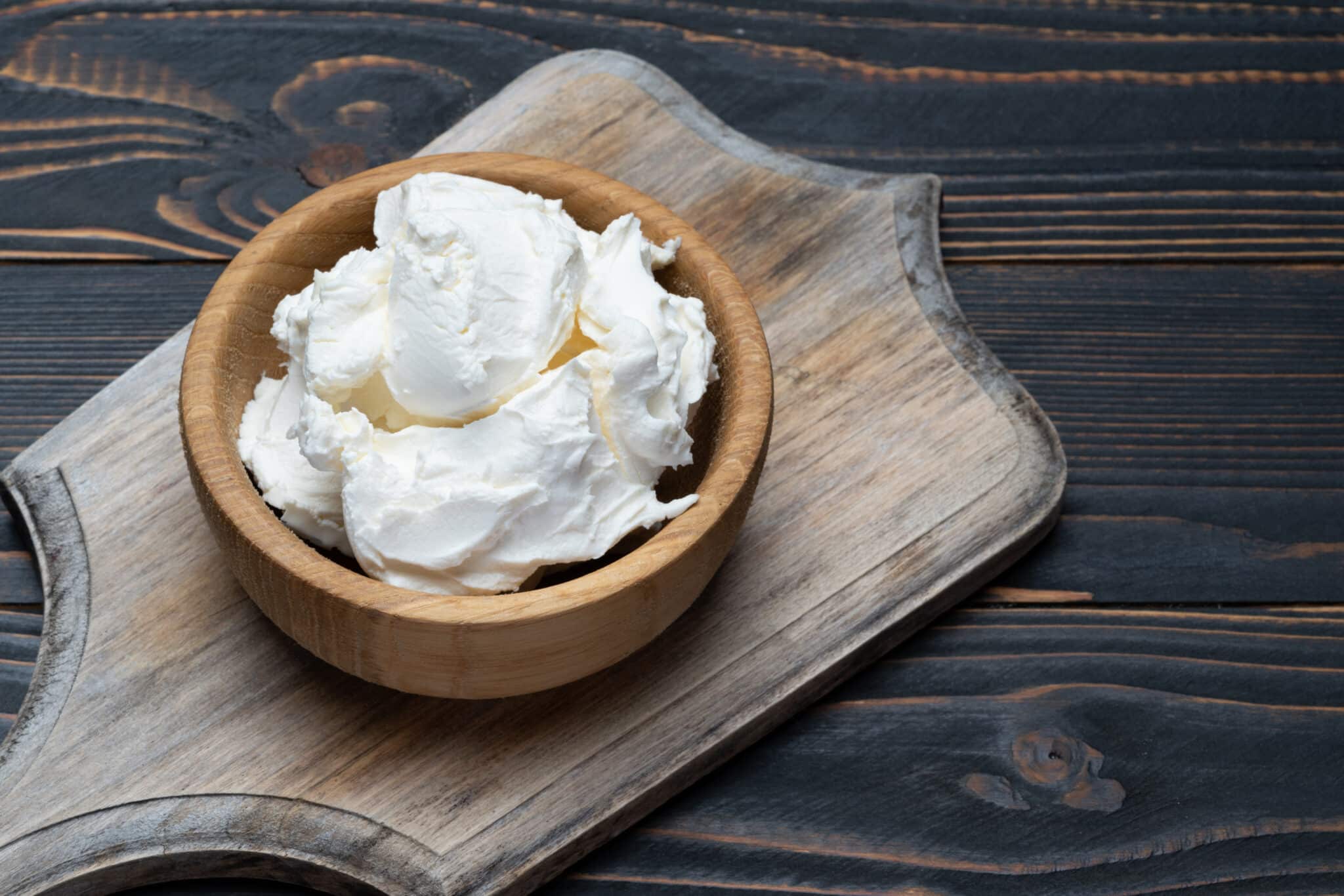 A bowl of mascarpone as a substitute for burrata cheese on a wooden cutting board.