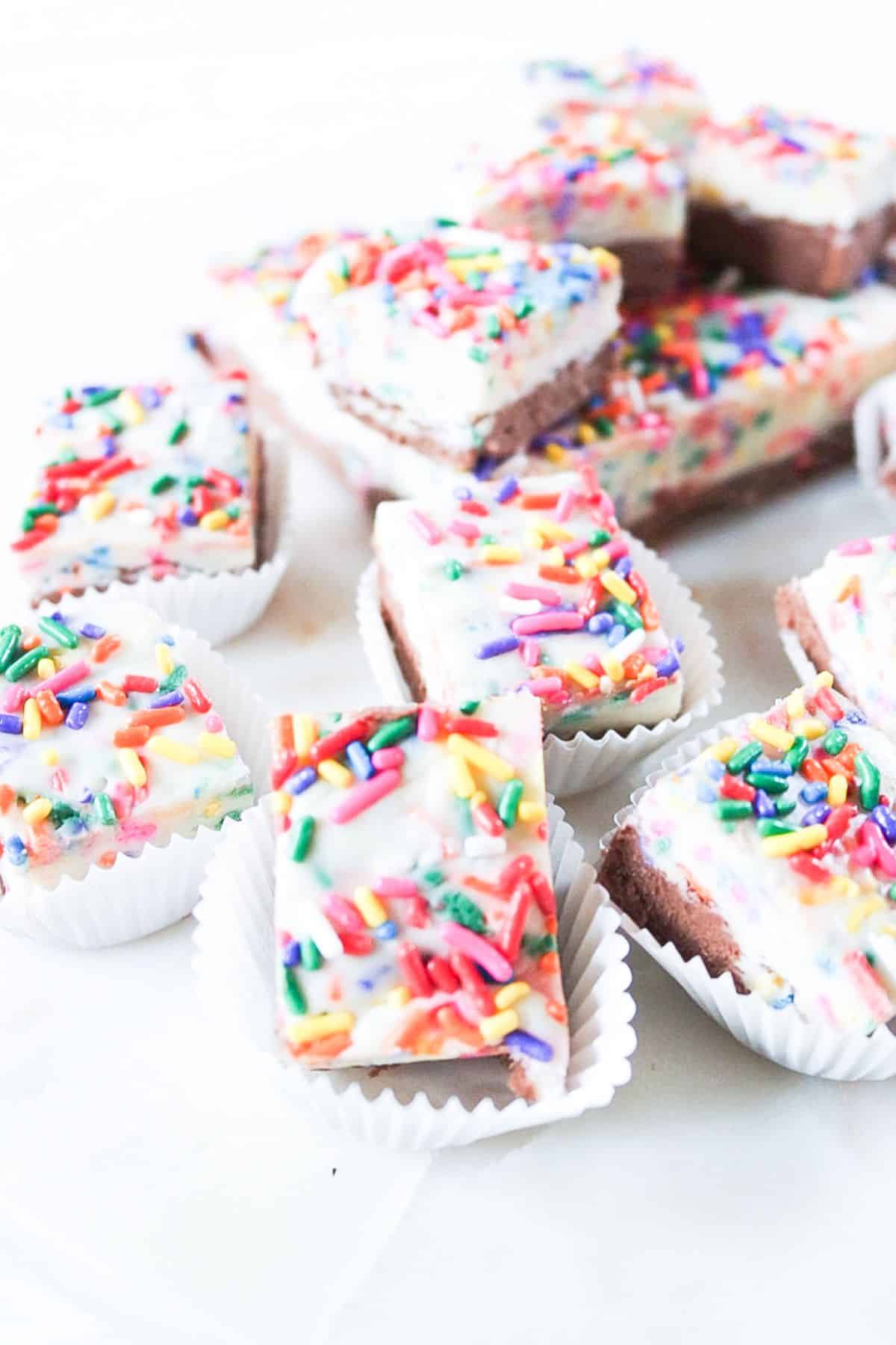 Funfetti fudge bars with sprinkles on a white plate and in paper muffin cups.