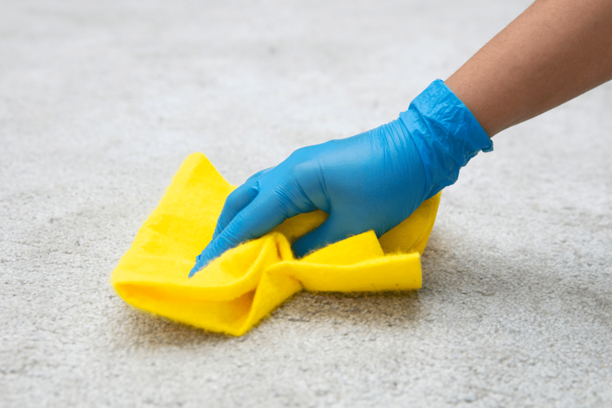 A person cleaning the carpet with a yellow cloth to remove a coffee stain.