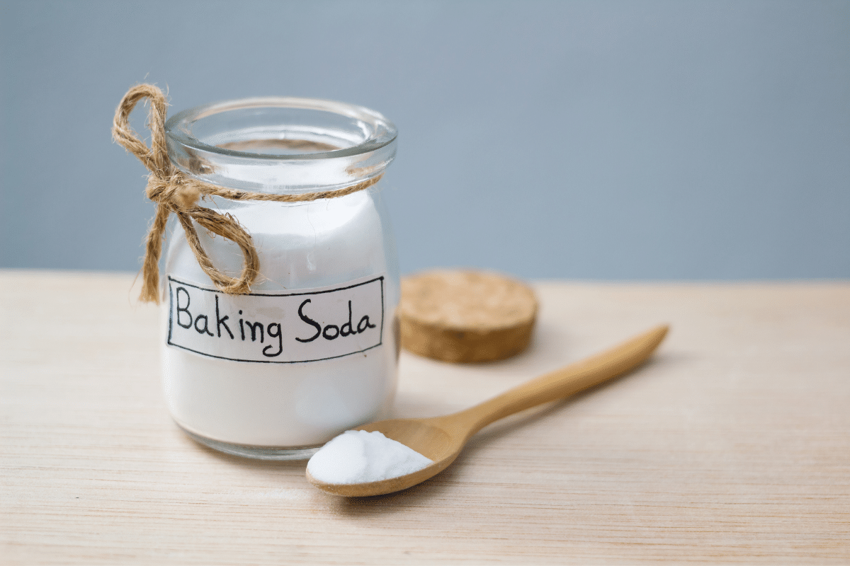 A jar of baking soda placed near a spoon as part of the solution to remove red wine stains from the carpet.