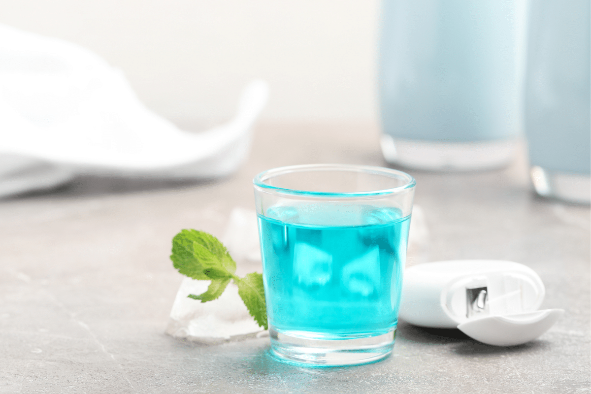 A glass of mouthwash with floss on the side.