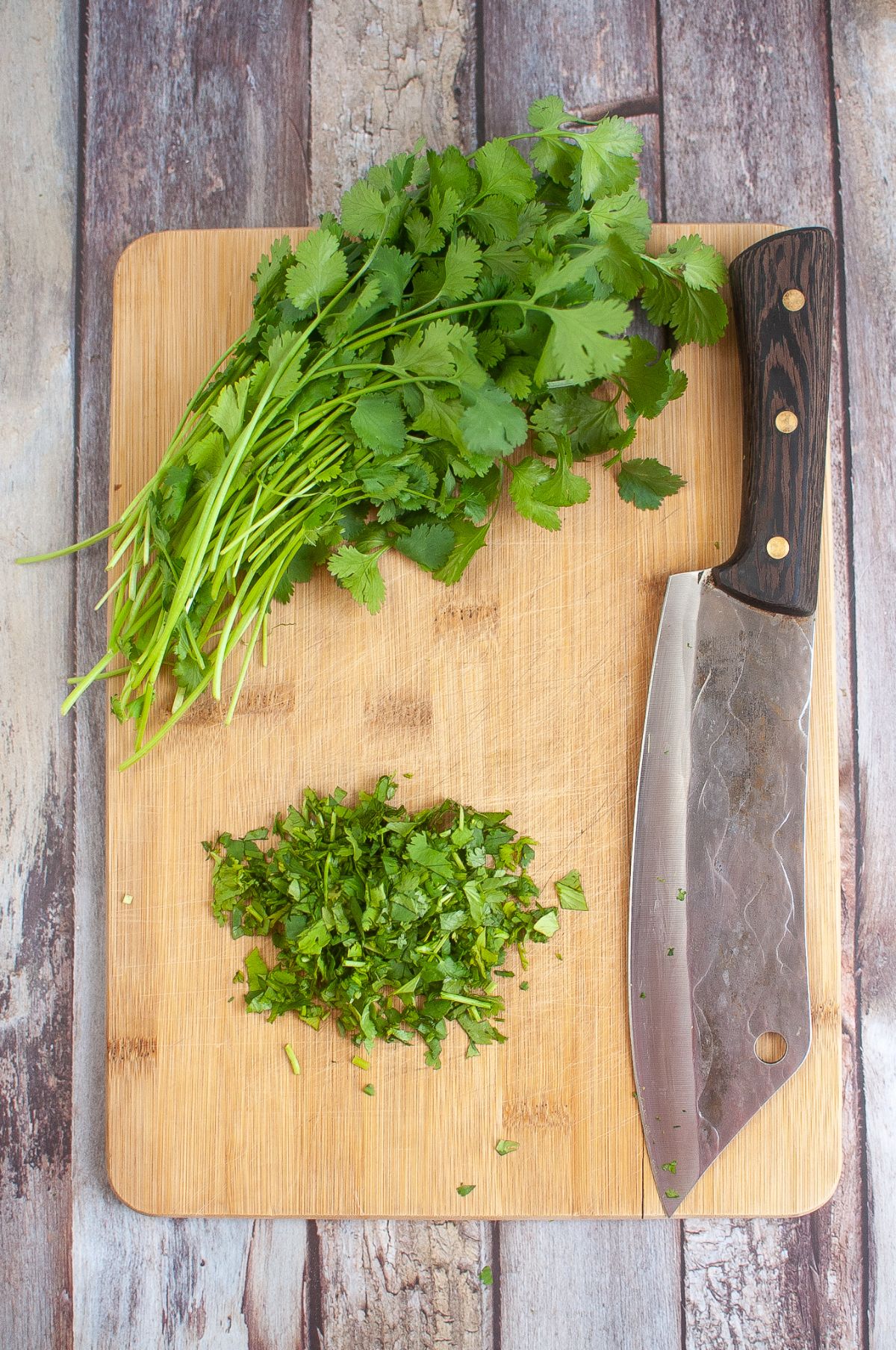 A cutting board with a knife and fresh cilantro.