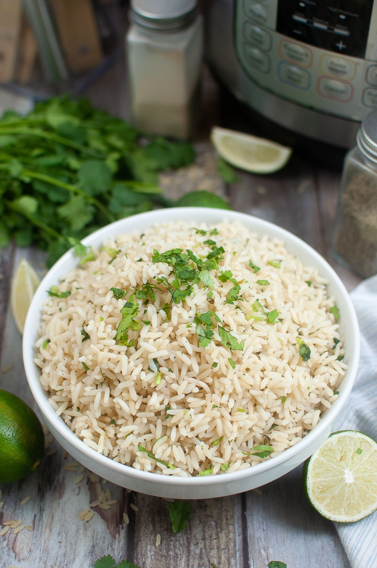 Instant pot rice pilaf in a bowl, garnished with cilantro with Limes and instant pot on the side.