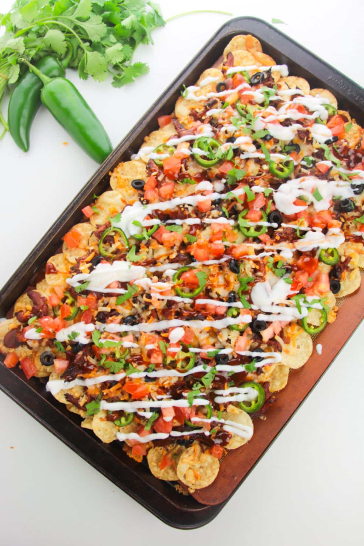 Pulled Pork Nachos on a baking sheet topped with bbq sauce and sour cream.