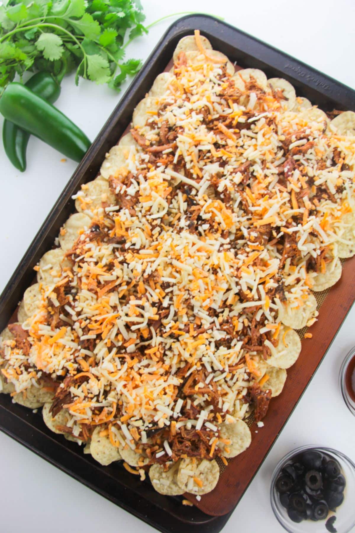 Tortilla chips with pulled pork and shredded cheese on a baking sheet.