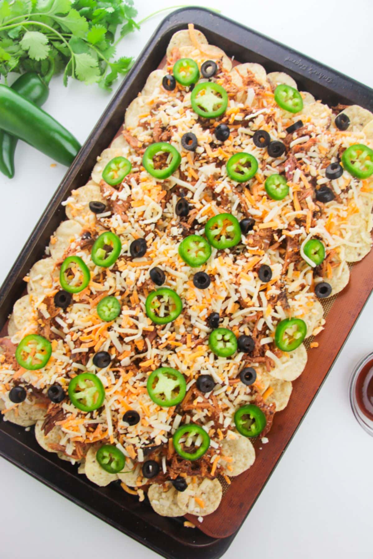 Black olives and jalapeno peppers are added to the tortilla chips with shredded cheese.