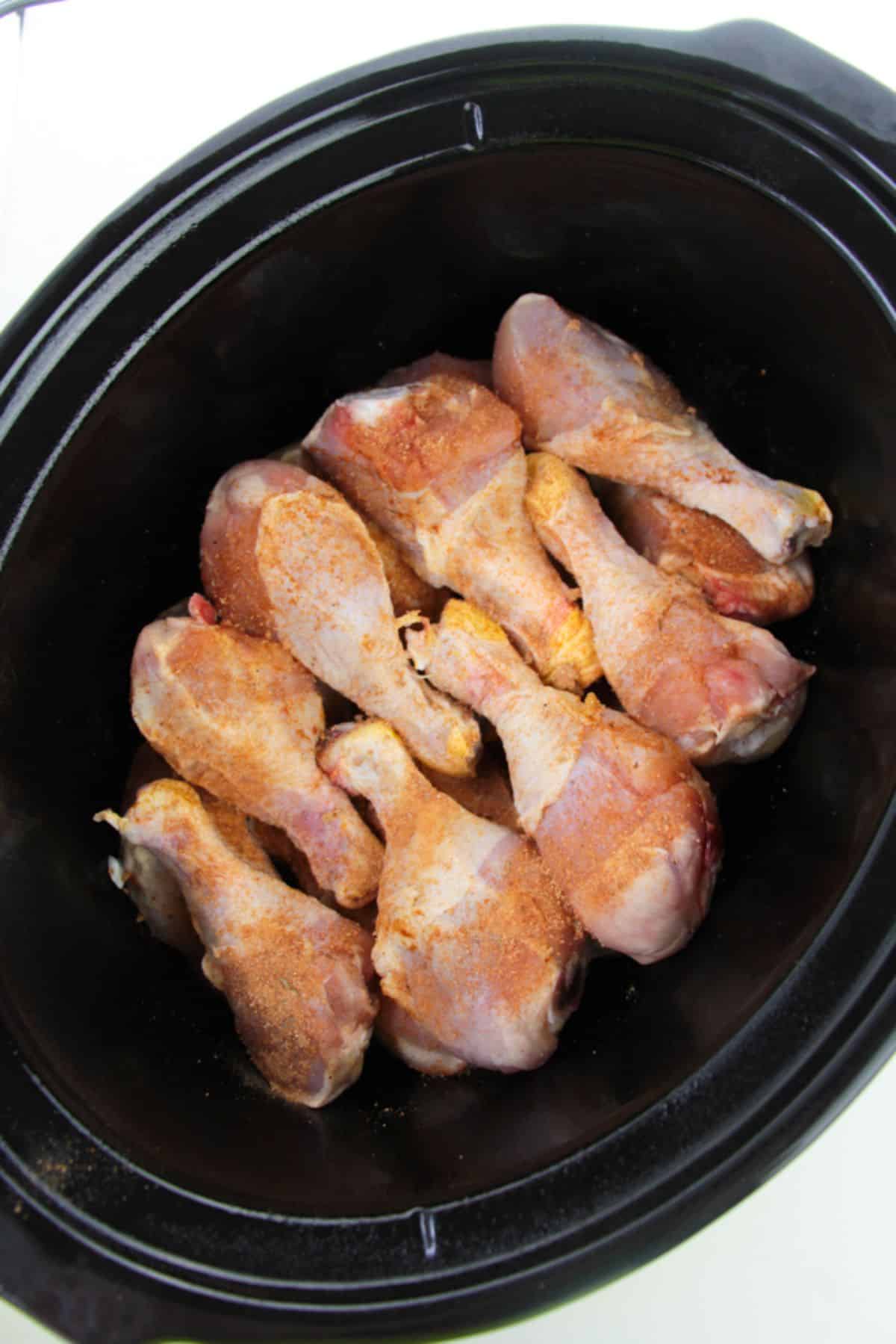 Rotisserie seasoning is added to the chicken legs inside the slow cooker.