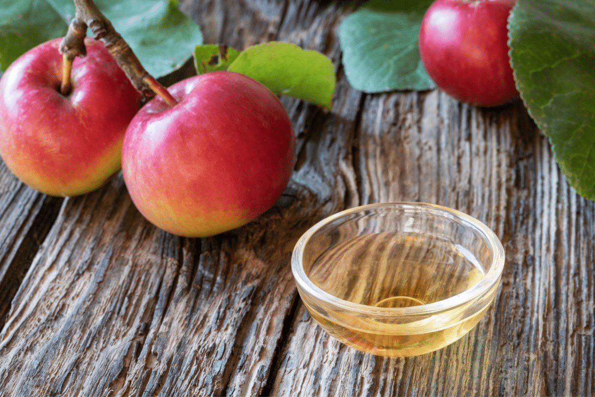 A bowl of apple cider vinegar, a substitute for champagne vinegar, and apples on a wooden table.