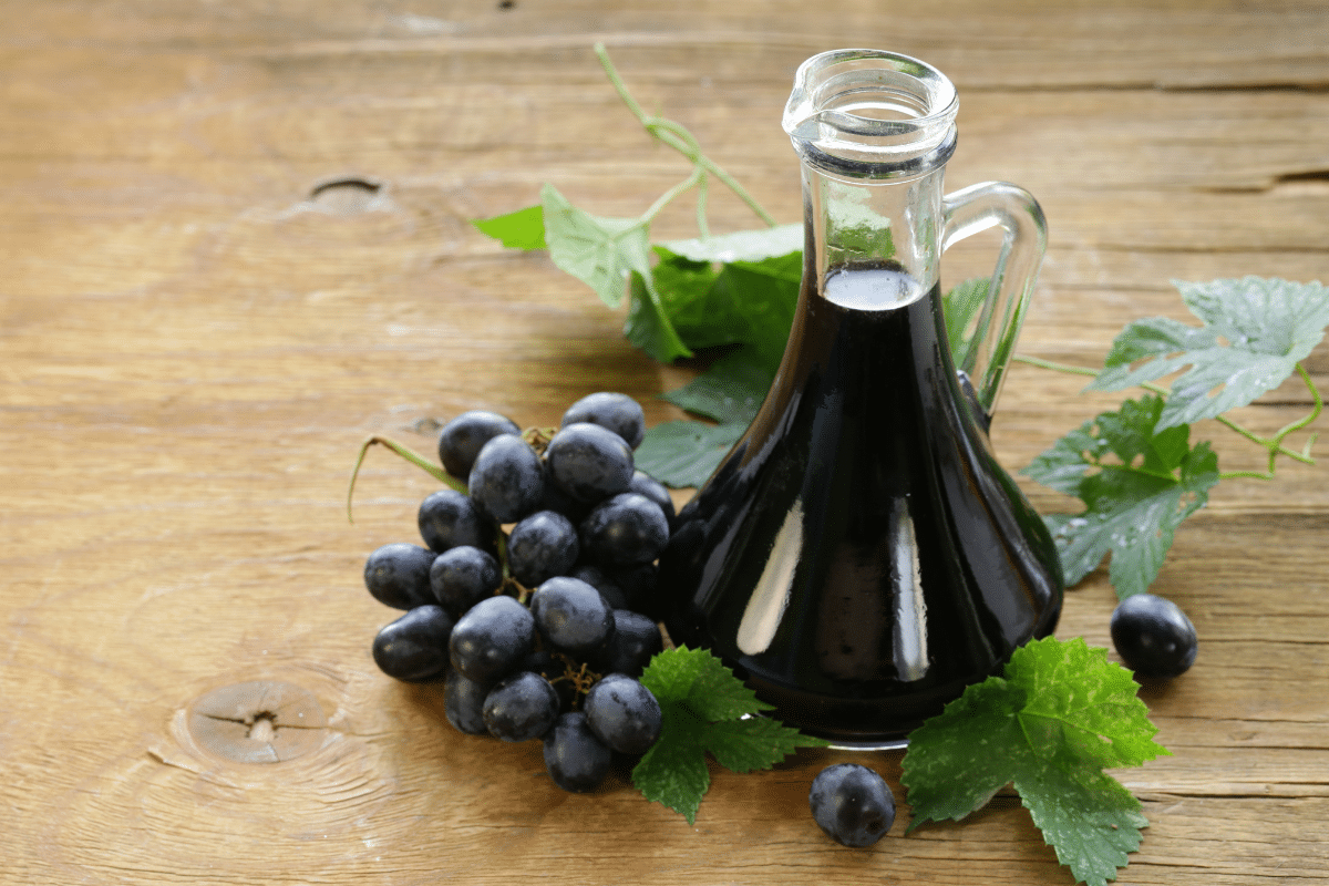 A bottle of balsamic vinegar, a substitute for champagne vinegar, and grapes on a wooden table.