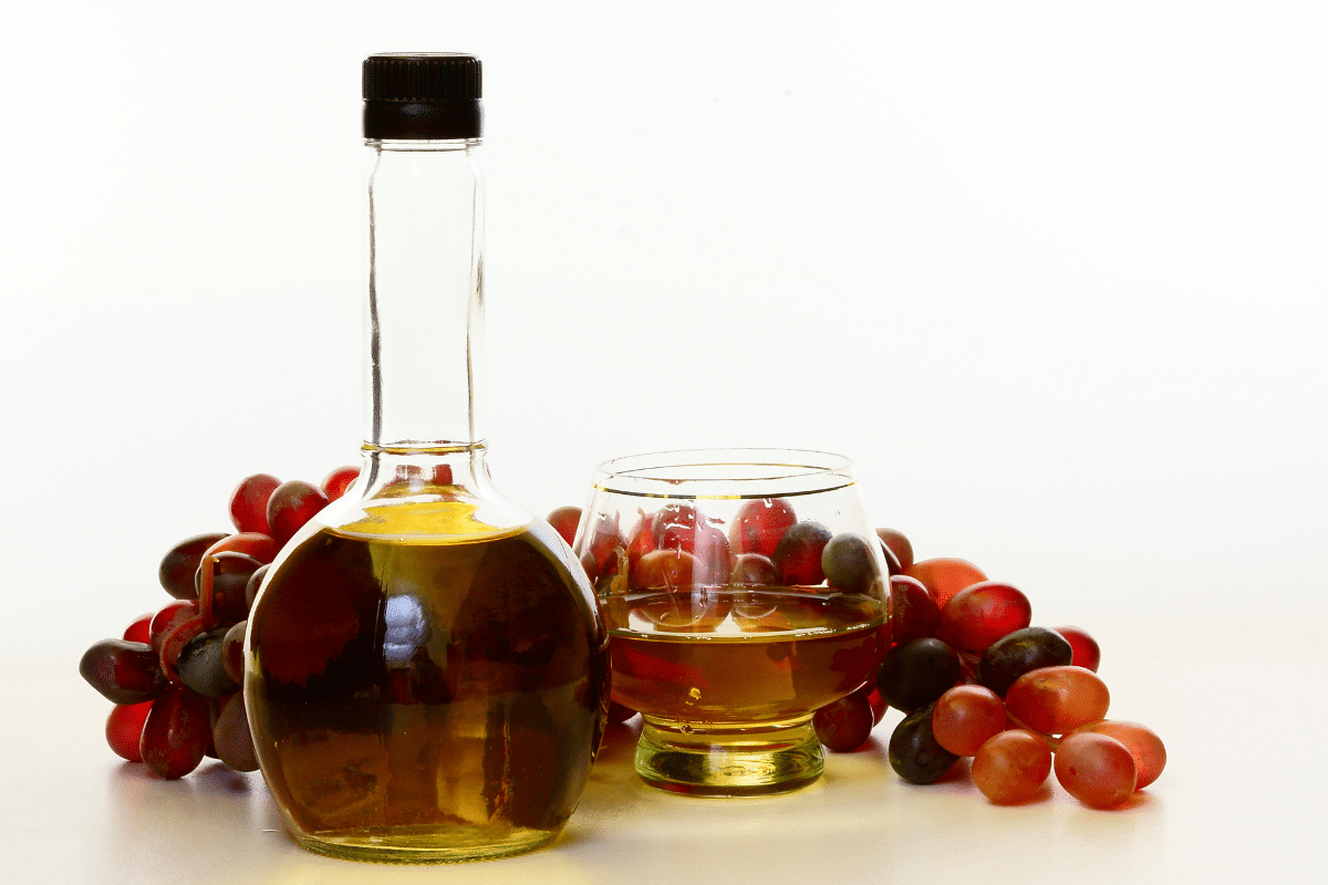 A glass and bottle of champagne vinegar with grapes on the side.