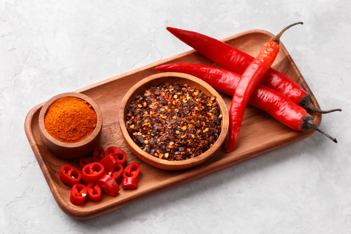 Chili flakes and chili powder, a substitute for chili sauce, displayed on a wooden tray.