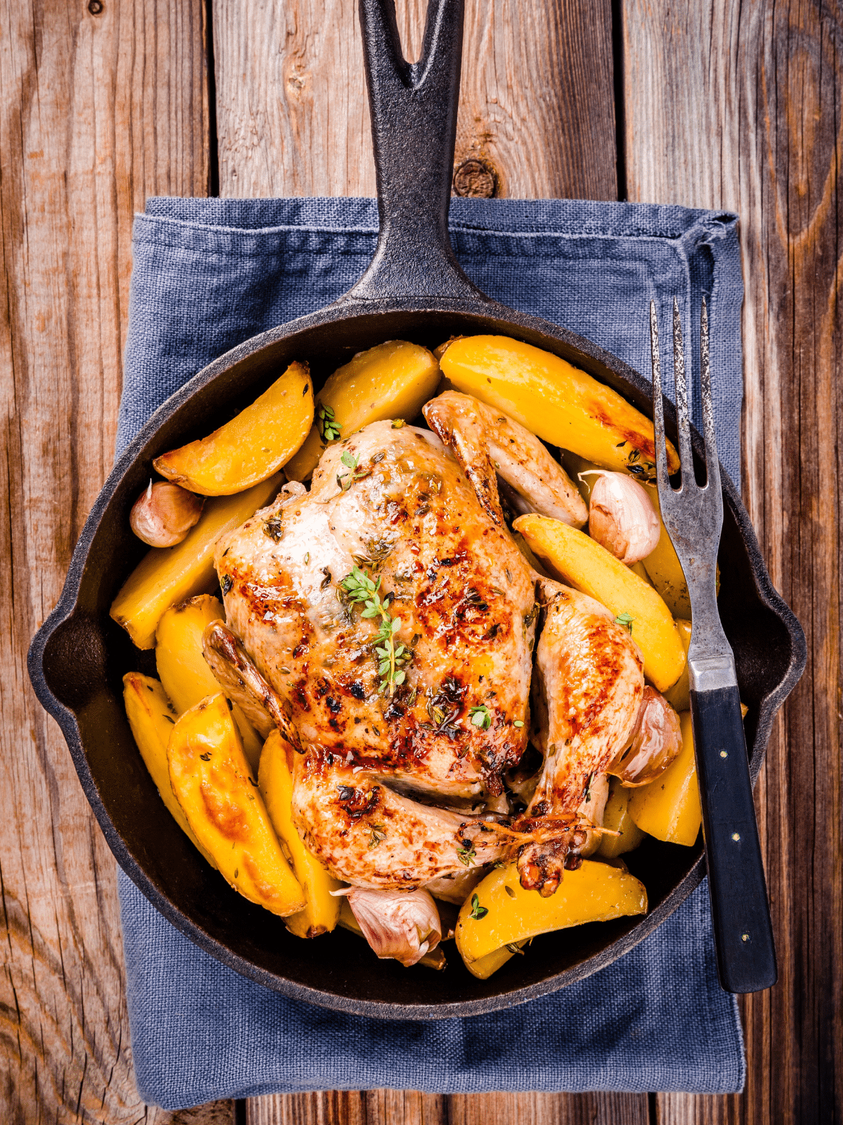 Chicken and potatoes served in a skillet on a wooden table.