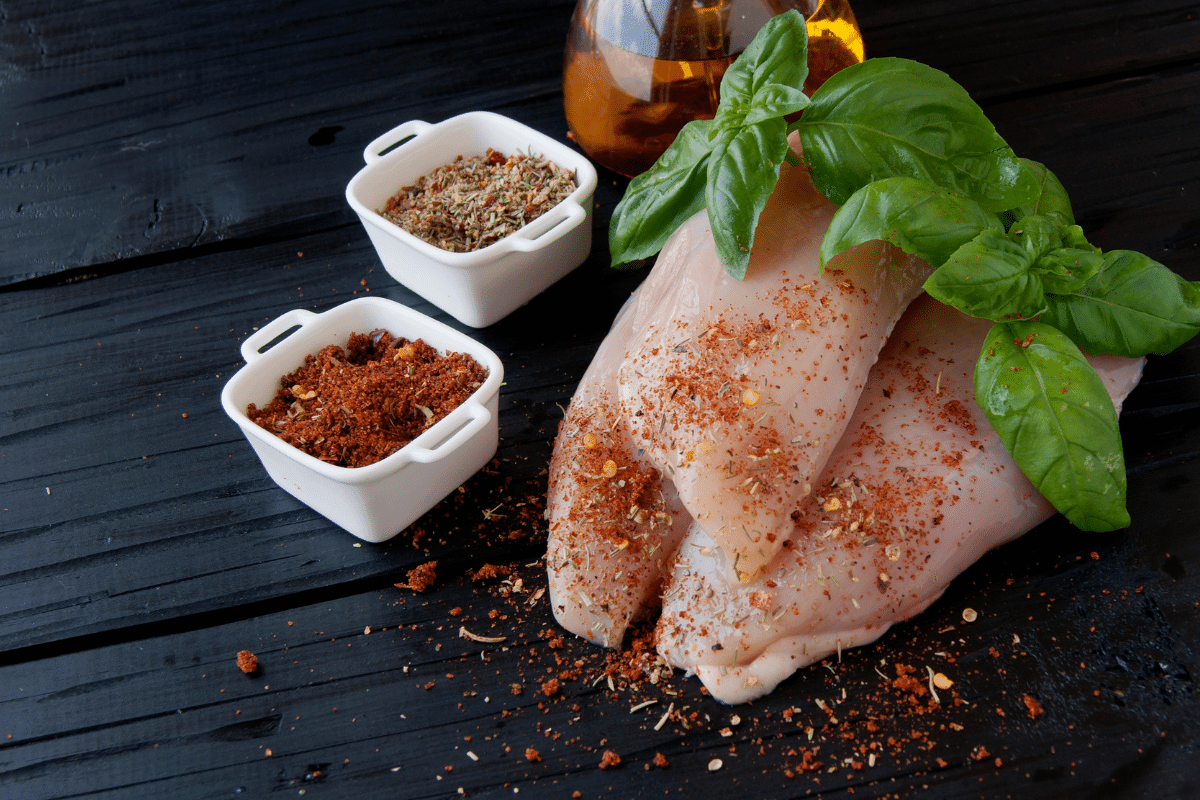 Spiced chicken breasts with herbs on a rustic wooden table, featuring a substitute for poultry seasoning.