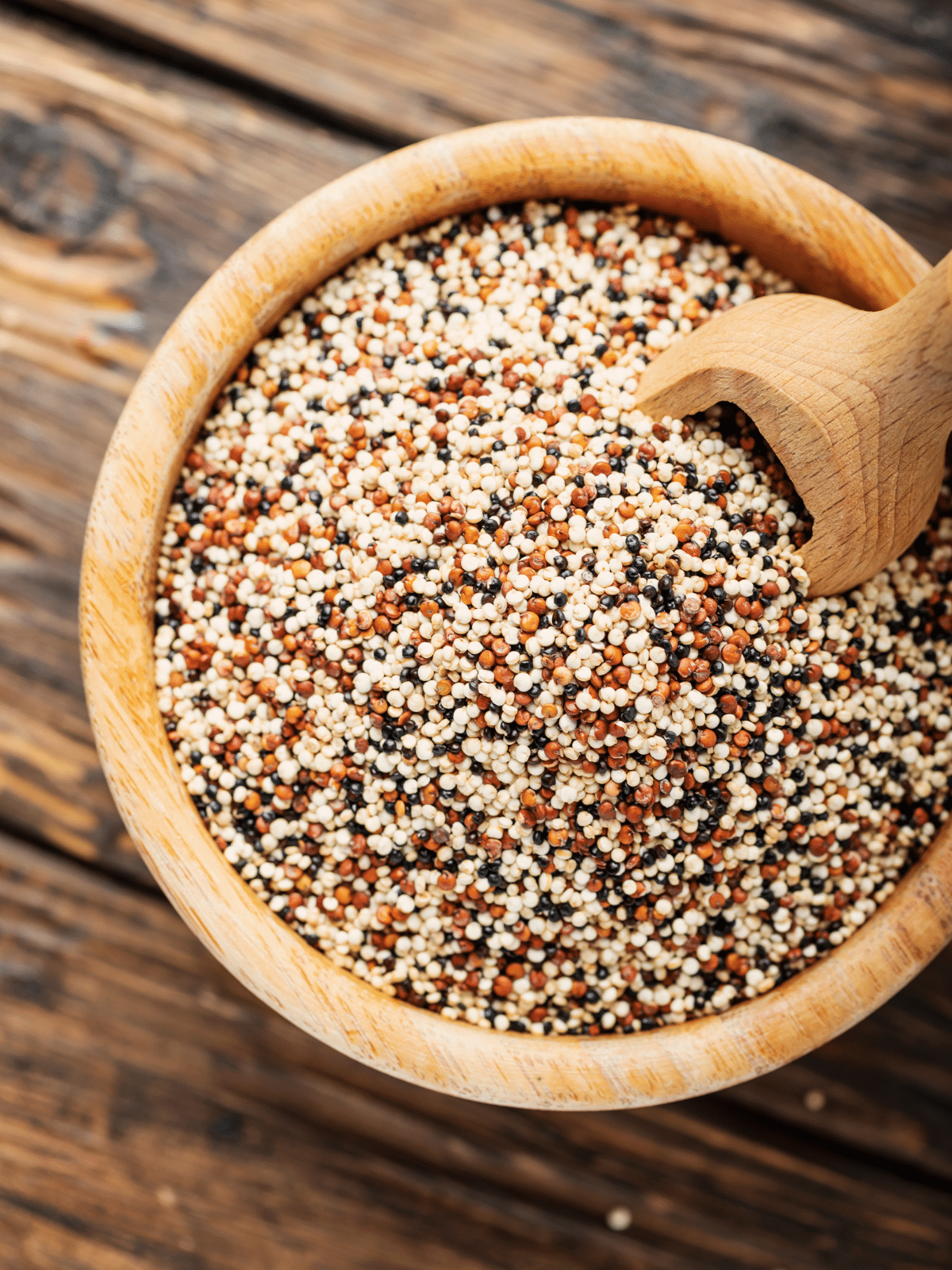 Quinoa in a wooden bowl with scoop in it on a wooden table.