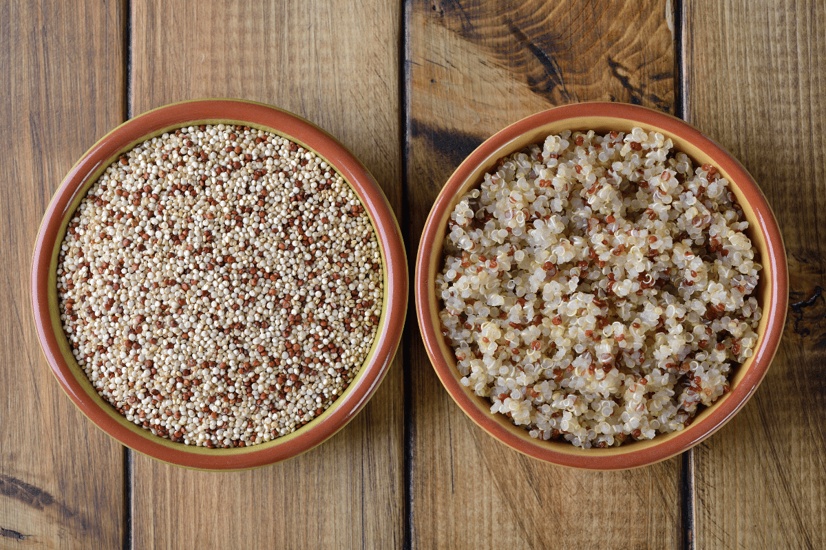 Two bowls of uncooked and cooked quinoa on a wooden table.