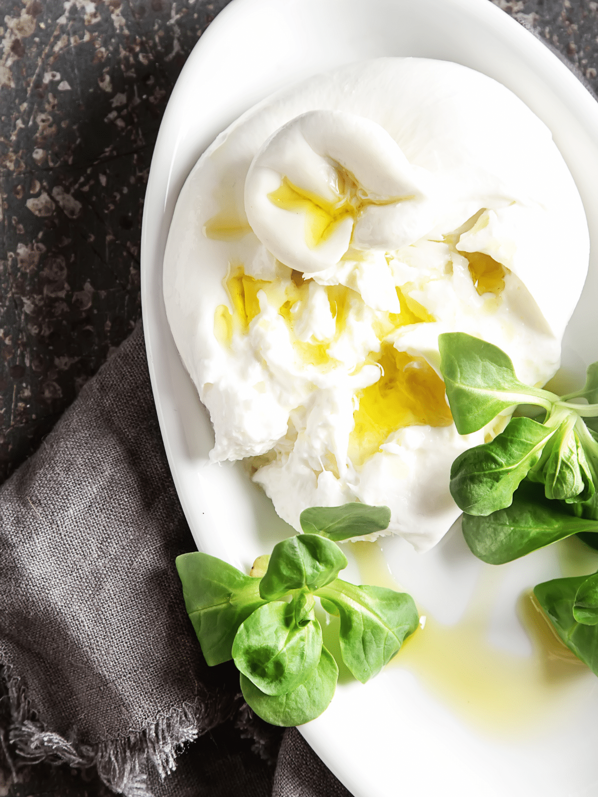 close up of A plate of burrata cheese with basil leaves and olive oil.